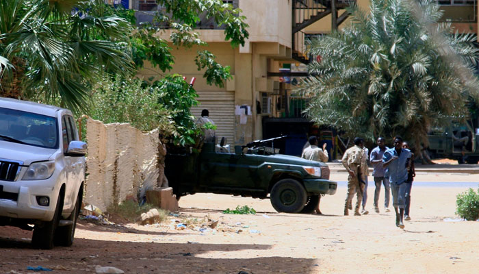 People walk past a military vehicle in Khartoum on April 15, 2023, amid reported clashes in the city. Sudans paramilitaries said they were in control of several key sites following fighting with the regular army on April 15, including the presidential palace in central Khartoum. — AFP