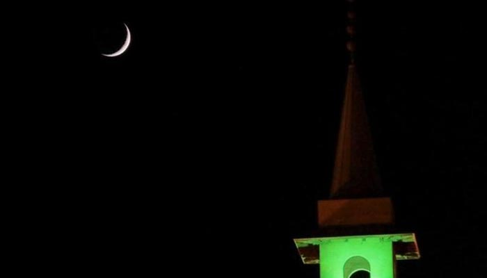 A new crescent seen through a telescope shines beside the tower of a mosque. — Reuters/File