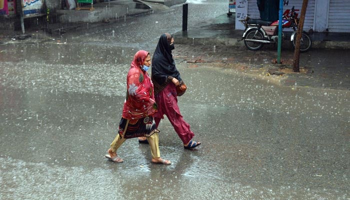 Women on their way at a road during heavy rain in Faisalabad on March 24, 2023. — Online