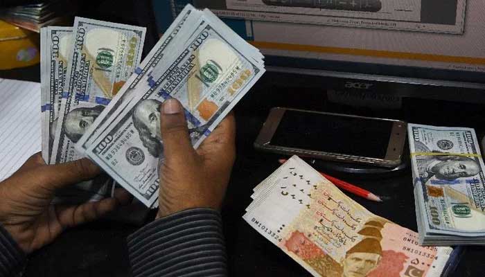 A person counting US dollars while rupee notes and a bundle of the foreign currency are seen in the background — AFP/File