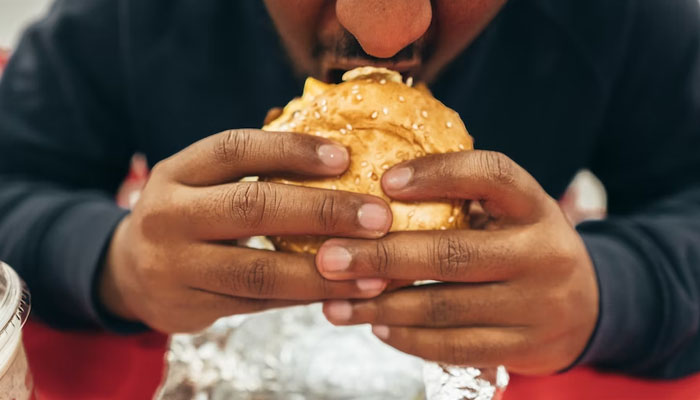 A person can be seen eating a burger. — Unsplash/File