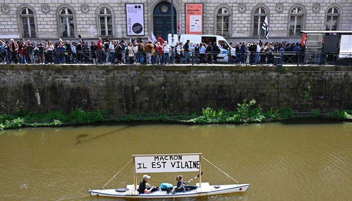 Protesters paddle a canoe with a sign which reads Macron, he is a villain during a demonstration on May Day (Labour Day). — AFP