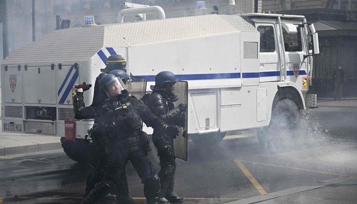 A French Riot Policeman standing next to a police water cannon throws a tear gas grenade towards protesters during a demonstration on May Day. — AFP