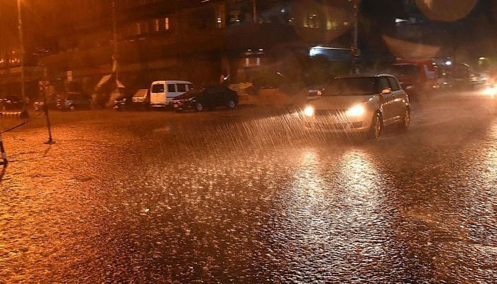 A file photo of vehicles passing through accumulated rain water during rain in Karachi. — INP