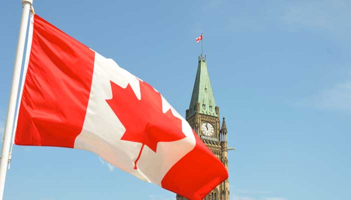 Canadian flag waves in front of a national monument. — Unsplash