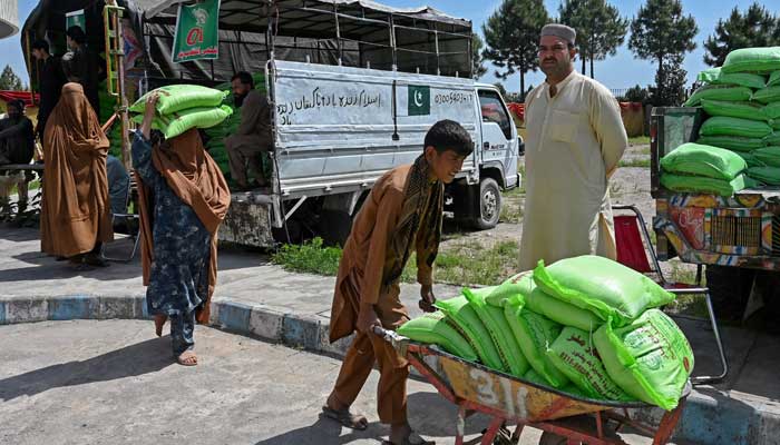 People leave after collecting free bags of flour from a government distribution point in Peshawar on April 10, 2023. — AFP