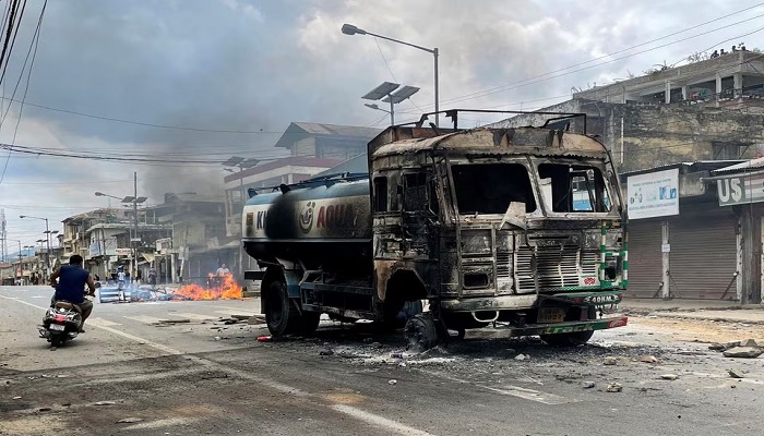 A scooterist rides past a damaged water tanker that was set afire during a protest by tribal groups in Churachandpur in the northeastern state of Manipur, India. — Reuters