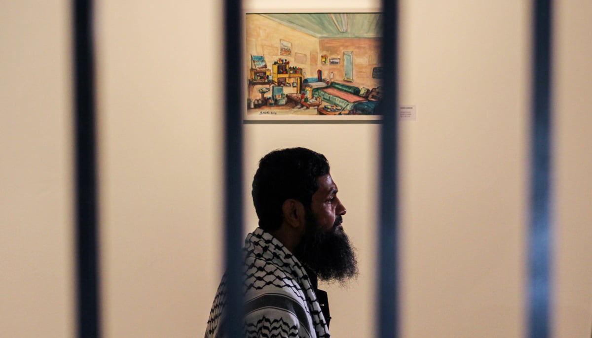 Ahmed stands before a painting he made portraying his room in Guantanamo Bay with rails of IVS art gallery in the foreground. — Photo by Hassaan Ahmed