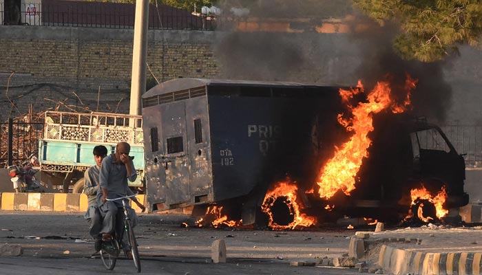 Men on a bike ride past a burning police vehicle during a protest by PTI activists and supporters of former prime minister Imran Khan against the arrest of their leader, in Quetta on May 9, 2023. — AFP