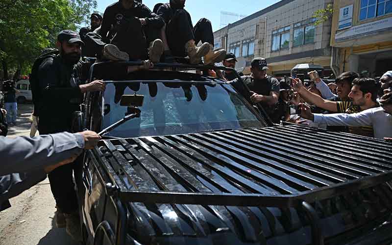 پاکستان کے سابق وزیر اعظم عمران خان کو 9 مئی 2023 کو اسلام آباد میں ہائی کورٹ پہنچنے پر سیکیورٹی اہلکار ایک کار کو لے جا رہے ہیں۔ — AFP