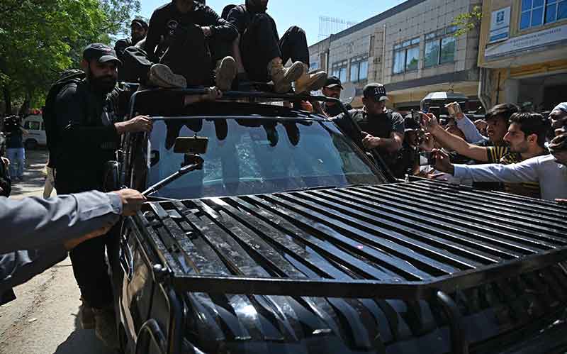 Security personnel escort a car carrying Pakistan´s former Prime Minister Imran Khan as he arrives at the high court in Islamabad on May 9, 2023. — AFP