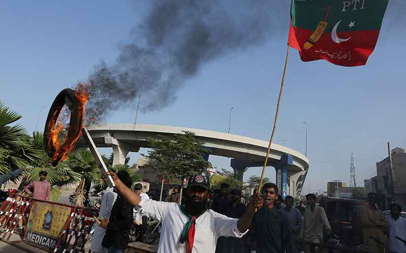 پاکستان تحریک انصاف پارٹی کا ایک کارکن اور پاکستان کے سابق وزیر اعظم عمران کا حامی 9 مئی 2023 کو ملتان میں اپنے رہنما کی گرفتاری کے خلاف احتجاج کے دوران جلتا ہوا ٹائر اور پارٹی پرچم تھامے ہوئے ہے۔