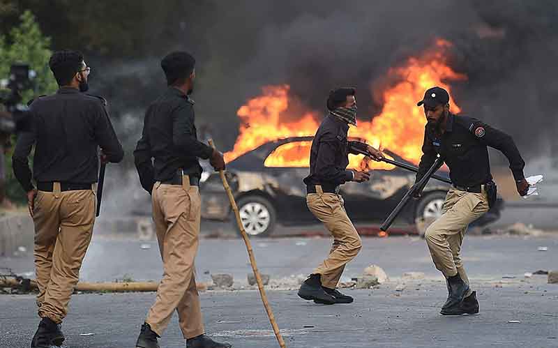 Policemen retreat after firing teargas shells towards Pakistan Tehreek-e-Insaf (PTI) party activists and supporters of former Pakistan´s Prime Minister Imran near burning car during a protest against the arrest of their leader in Karachi on May 9, 2023.