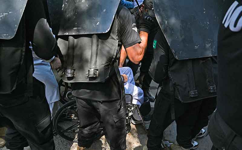 Security personnel escort Pakistan´s former Prime Minister Imran Khan (unseen) sitting on a wheelchair at the High Court in Islamabad on May 9, 2023