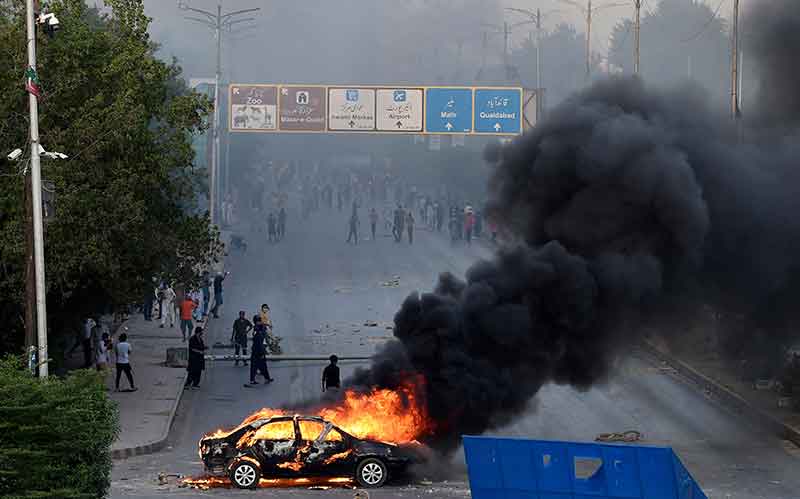 A car is seen burning along a road as Pakistan Tehreek-e-Insaf (PTI) party activists and supporters of former Pakistan´s Prime Minister Imran block a road during a protest against the arrest of their leader in Karachi on May 9, 2023. — AFP