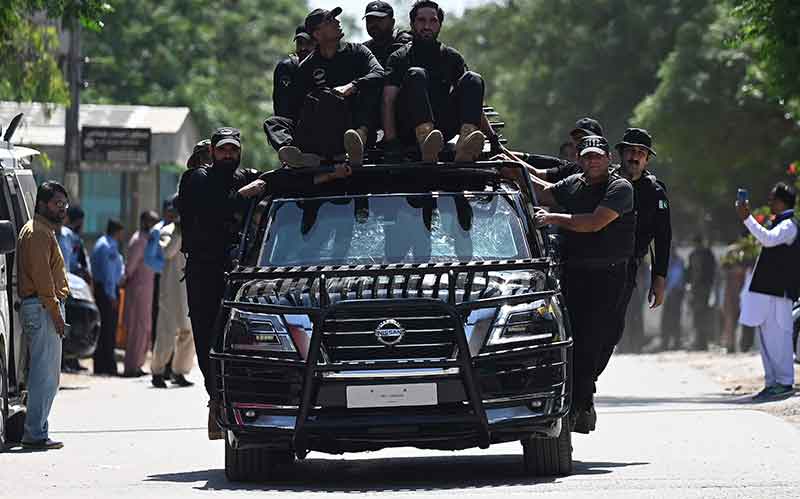 پاکستان کے سابق وزیر اعظم عمران خان کو 9 مئی 2023 کو اسلام آباد میں ہائی کورٹ پہنچنے پر سیکیورٹی اہلکار ایک کار کو لے جا رہے ہیں۔ — AFP