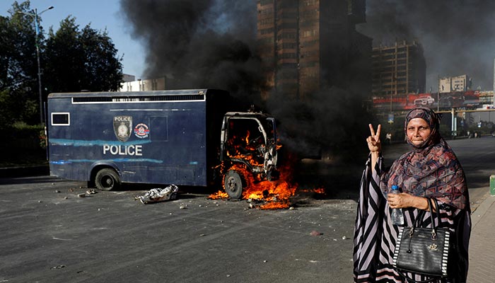 A woman gestures next to a burning police vehicle during a protest by supporters of former Prime Minister Imran Khan after his arrest, in Karachi, May 9, 2023. — Reuters