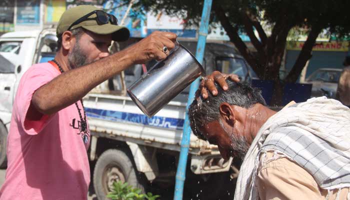 12 مئی 2023 کو کراچی میں شدید درجہ حرارت کے دوران ایک رضاکار مزدور کے سر پر اسے ہیٹ اسٹروک سے بچانے کے لیے پانی کی بارش کر رہا ہے۔ — آن لائن
