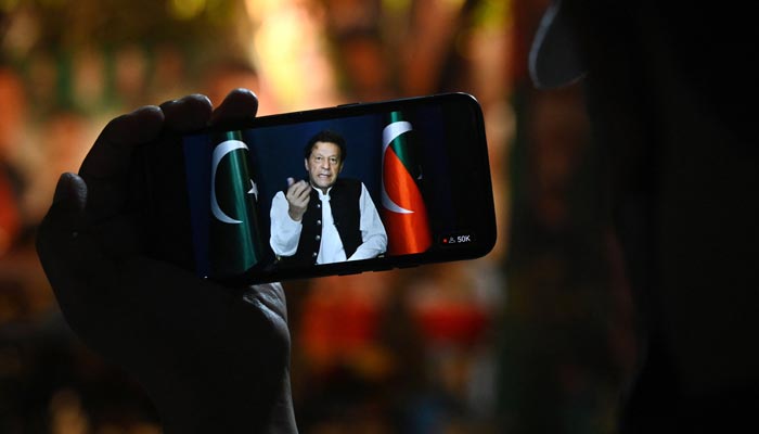An activist of PTI party listens to former prime minister Imran Khans speech on a phone, in Zaman Park in Lahore on May 13, 2023. — AFP