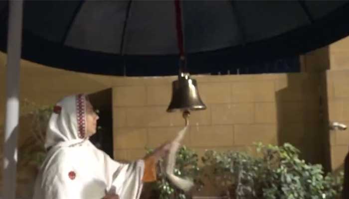 A woman is ringing a bell of hope installed outside the Gate No 1 of the Governor House in Karachi in this still taken from a video — Twitter/@psec_governor