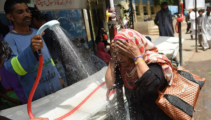 A volunteer showers a woman with water during a heatwave in Karachi. — AFP/File