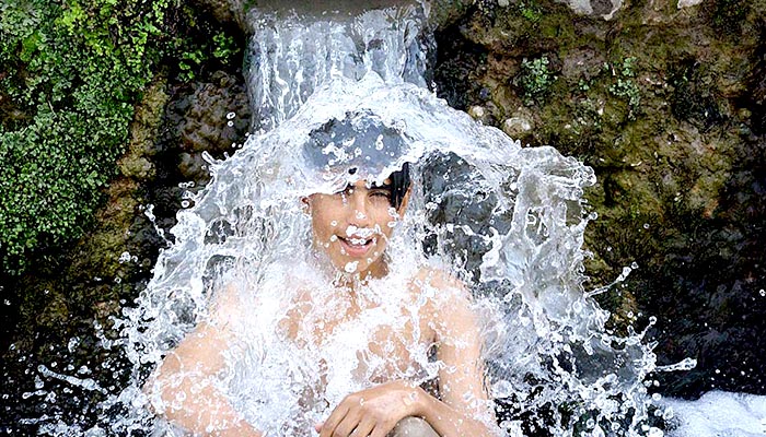 A boy enjoys a bath under stream water to get relief from the hot weather in Peshawar on May 3, 2023. — APP