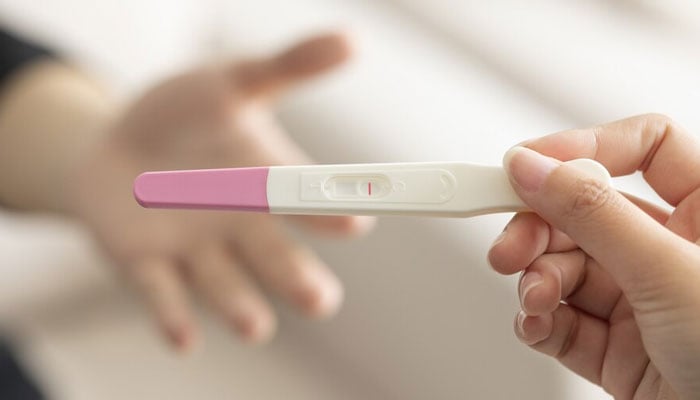 Closeup of a womans hand holding up a pregnancy test kit with a negative result. Freepik.com