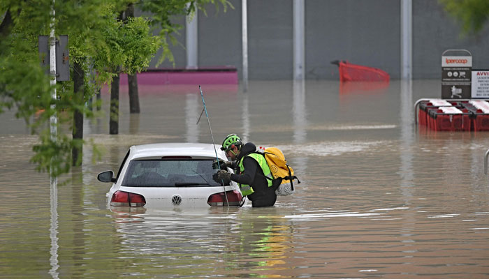 A speleological alpine rescuer looks in a car for missing persons near a supermarket in a flooded area in Cesena on May 17, 2023. — AFP