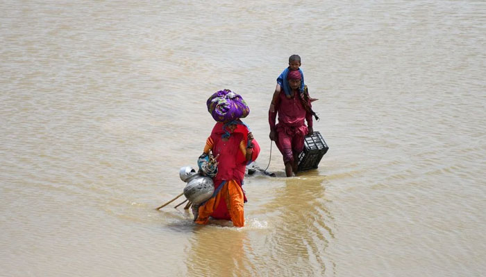 26 اگست 2022 کو جامشورو میں مون سون کے موسم کے دوران بارشوں اور سیلاب کے بعد ایک خاندان اپنے سامان کے ساتھ بارش کے پانی میں سے گزر رہا ہے۔ - رائٹرز