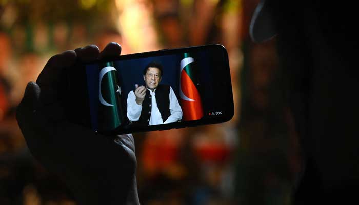 A PTI supporter listens to party Chairman Imran Khan´s speech on a phone, in Zaman Park in Lahore on May 13, 2023. — AFP