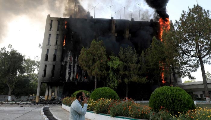 A man speaks on his mobile as fire and smoke billow from a Radio Pakistan building after it was set afire by the supporters of former prime minister Imran Khan during a protest against his arrest, in Peshawar, Pakistan, May 10, 2023. — Reuters