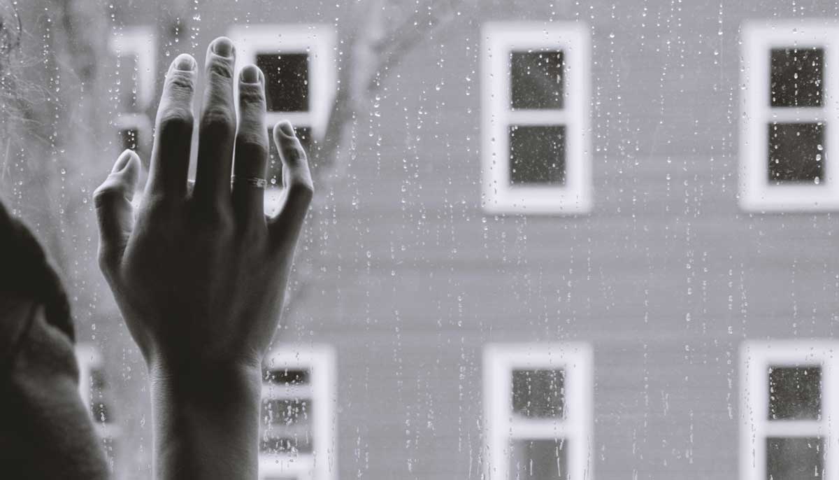 A representational image of a womans hand against a window in rainy weather. — Unsplash