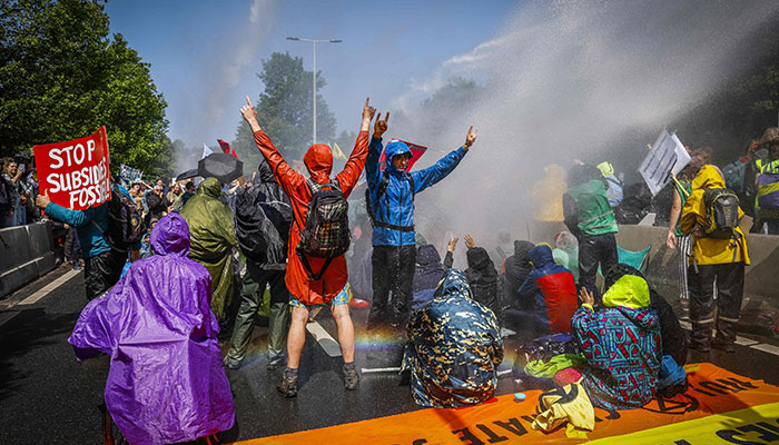 Extinction Rebellion (XR) activists shout slogans as police officials use a water cannon to disperse their protest while blocking the A12 autoroute in The Hague on May 27, 2023, to show the activists opposition to fossil subsidies given by the Dutch government. During the most recent blockade on March 11, some 700 activists were arrested.—AFP