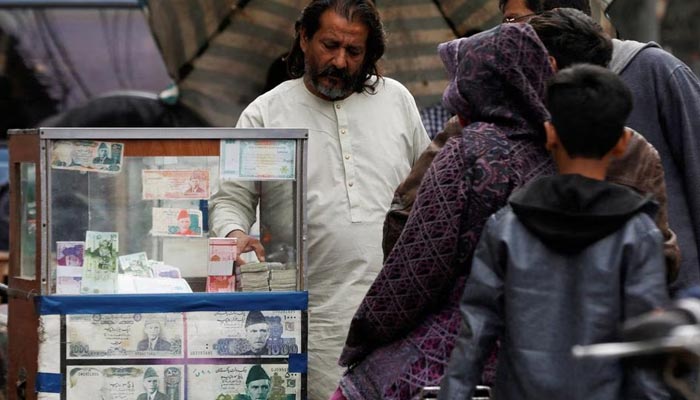 A currency broker stands near his booth, which is decorated with pictures of currency notes, while dealing with customers, along a road in Karachi on January 27, 2023. — Reuters