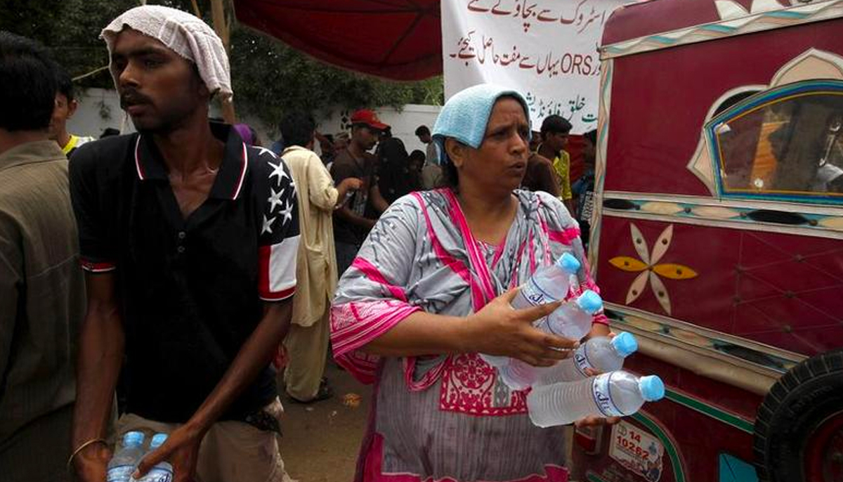 Volunteers cover their heads with water-soaked towels, to beat the heat, while distributing water bottles, outside Jinnah Postgraduate Medical Centre (JPMC) in Karachi, Pakistan, June 25, 2015. — Reuters