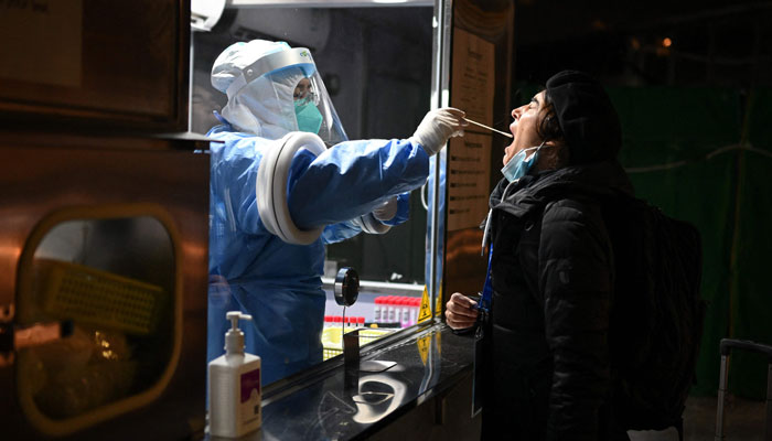 An employee, wearing a hazmat suit, collects a swab on a member of the media during a daily COVID-19 pcr test ahead of the 2022 Winter Olympics in Beijing on January 27, 2022. — AFP