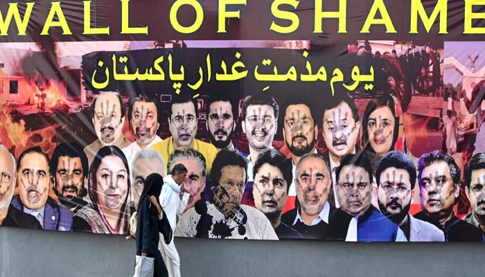 People walk past a wall poster denouncing former prime minister Imran Khan and his PTI party members, in Rawalpindi on May 27, 2023. — AFP