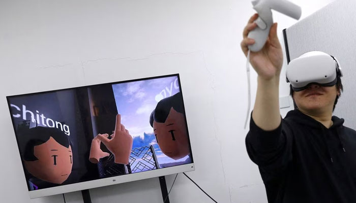 Pan Bohang, founder of vHome wearing Metas Oculus VR headset and uses a touch controller to high-five a virtual gathering, as a screen shows virtual content, at office in Beijing, China. —Reuters/File