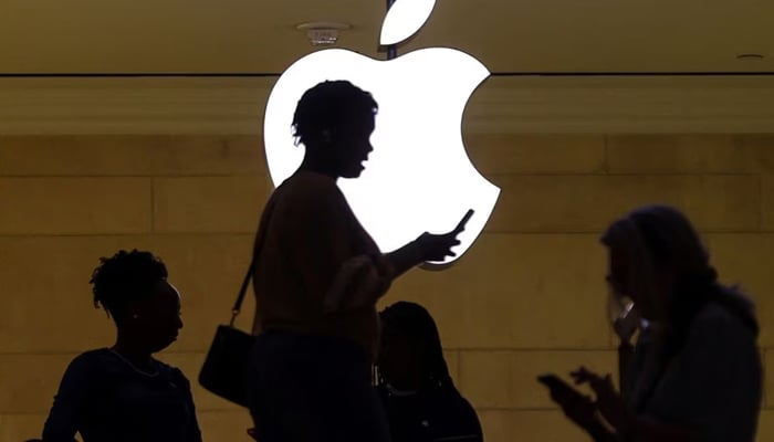 A women uses an iPhone mobile device as she passes a lighted Apple logo at the Apple store at Grand Central Terminal in New York City, U.S., April 14, 2023. — Reuters