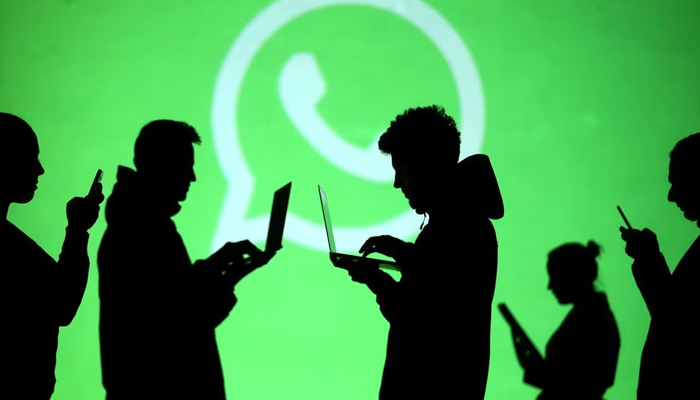 Silhouettes of laptop and mobile device users are seen next to a screen projection of Whatsapp logo in this picture illustration taken March 28, 2018. — Reuters