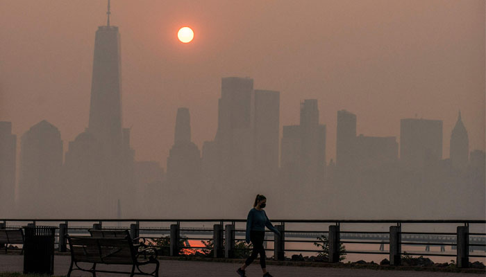 A woman walks as the sun rises behind One World Trade Center and the New York skyline, while smoke from Canada wildfires covers the Manhattan borough as it is seen from the Liberty State Park on June 8, 2023, in New Jersey. — AFP