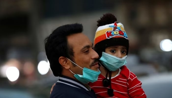 A man and child with protective masks walk outside a market in Karachi, Pakistan. — Reuters/File