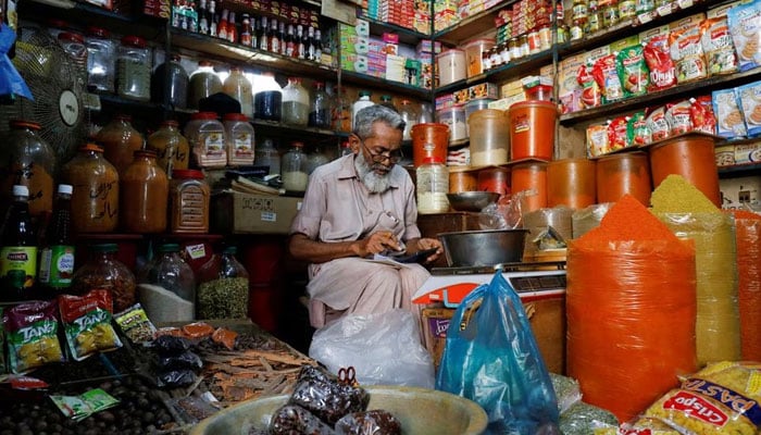 A shopkeeper uses a calculator while selling spices and grocery items along a shop in Karachi, Pakistan June 11, 2021. — Reuters