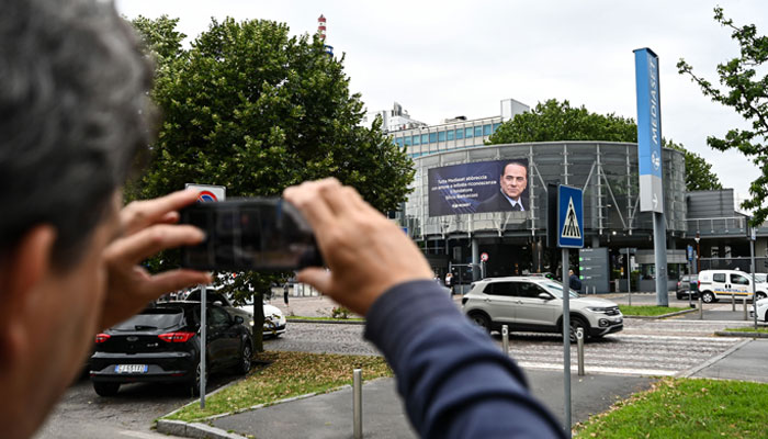 A man takes pictures of a giant banner bearing a portrait of late Italian former PM Silvio Berlusconi on the facade of the Mediaset headquarters in Cologno Monzese, Italy on June 12, 2023. — AFP