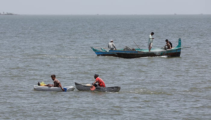 Boys sail, while people on a fishing boat prepare to catch fish, after a ban was imposed on coastal activities following the cyclonic storm, Biparjoy, over the Arabian Sea, at the Ibrahim Hyderi fishing village on the outskirts of Karachi, on June 12, 2023. — Reuters