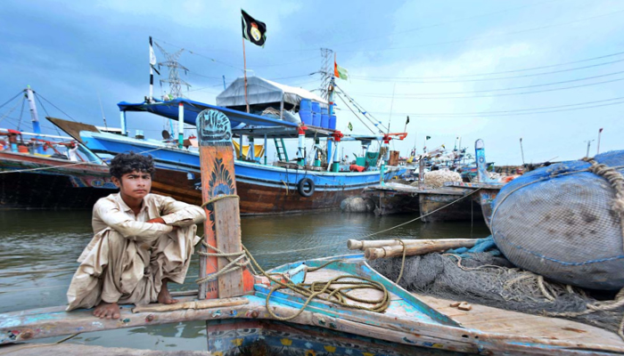 A fisherman sits on his boat anchored at the Ibrahim Hyderi jetty on June 15, 2023, after authorities issue alert regarding the effects of cyclone Biparjoy. — APP
