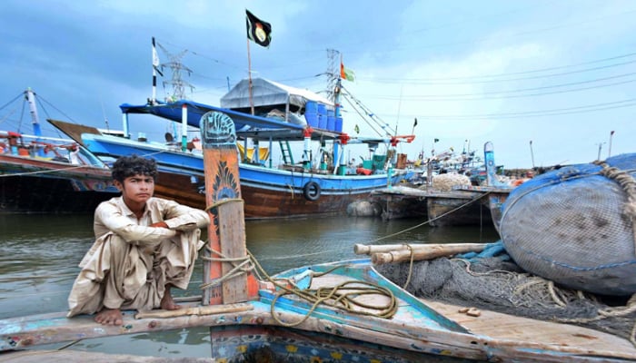 A fisherman sits on his boat anchored at the Ibrahim Hyderi jetty on June 15, 2023, after authorities issue alert regarding the effects of cyclone Biparjoy. — APP