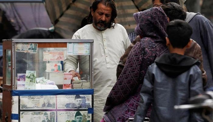 A currency broker stands near his booth, which is decorated with pictures of currency notes, while dealing with customers, along a road in Karachi, Pakistan January 27, 2023.