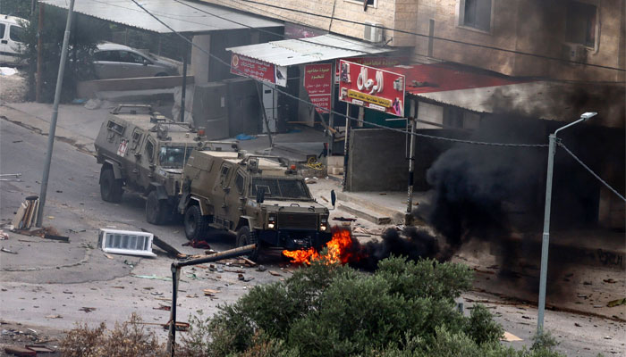 Tyres burn beneath Israeli security forces armoured vehicles during a raid in Jenin in the occupied West Bank on June 19, 2023. — AFP