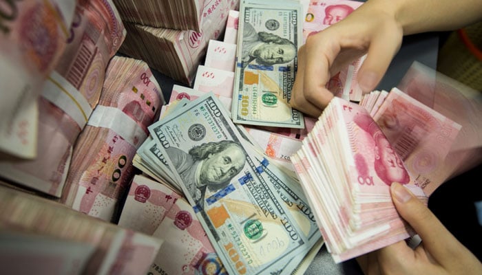 A person counts Chinese 100-yuan notes and US dollar bills at a bank counter. — AFP/File